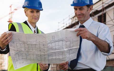 The Bill of Materials jpg of man and a woman, wearing hard hats, while looking at a drawing on a building site. 